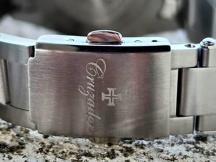 Fecho de aço escovado com a Cruz de Cristo e a assinatura Cruzador gravadas.